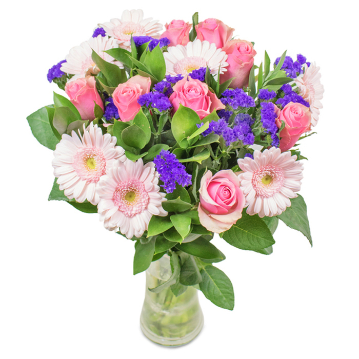 A visually captivating floral arrangement sits atop a pristine white backdrop, capturing the gentle elegance of Bayswater's unique blend of sophistication and laid-back charm. The bouquet's focal point is a carefully harmonized mix of approximately 7-9 medium and soft pink roses-some tenderly furled, others opening in classic spiral formation-paired with 5-7 pale pink gerbera daisies whose large, circular heads radiate warmth and subtle confidence. Interwoven clusters of vivid purple statice or limonium create inviting textural contrast and pops of deeper colour, reminiscent of Bayswater's vibrant mews and hidden gardens. Abundant, deep green foliage forms a rich undercurrent, enhancing the bouquet's freshness and hinting at the local woodlands and parks just beyond the high streets. Transparent glass reveals clean stems submerged in clear water, inviting contemplation of both natural beauty and expert local craftsmanship. Ideal for milestones from birthdays to anniversaries, Mother's Day surprises, or as a welcoming centrepiece for a Westbourne Grove townhouse, this arrangement crafted by Flower Delivery Bayswater radiates affection, celebration, and a true spirit of local joy.